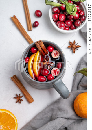 A cup of red mulled wine with cinnamon, orange and cranberry on a light background A cup of red mulled wine with cinnamon, orange and cranberry on a light background 136228917