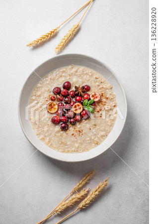Oatmeal with cranberry, cinnamon and spicy  in a plate on a light background with dry ears of wheat. 136228920