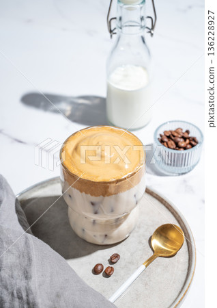 Dalgona coffee on a marble background with bottle, coffee beans, spoon and morning shadow 136228927