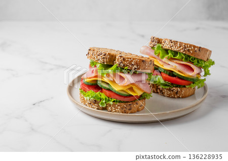 Two sandwiches with ham, cheese, lettuce, vegetables and seeded bread on a plate 136228935
