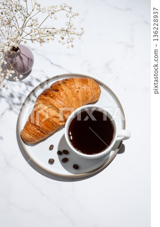 Freshly brewed black coffee in a cup and croissant on a plate on a white marble background 136228937
