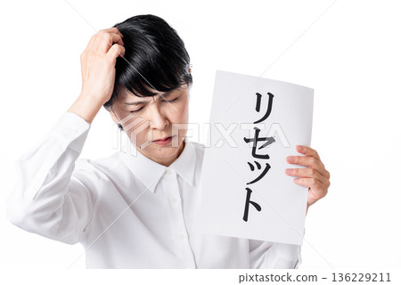 A senior woman holding a piece of paper with the word "reset" written on it and holding her head A senior woman holding a piece of paper with the word "reset" written on it and holding her head 136229211