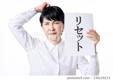 A senior woman with a displeased expression holding a piece of paper that says "reset" A senior woman with a displeased expression holding a piece of paper that says "reset" 136229213