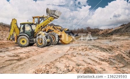 A construction site or sand pit with two powerful wheeled front loaders ready to go, under partly cloudy skies during the day A construction site or sand pit with two powerful wheeled front loaders ready to go, under partly cloudy skies during the day 136229593