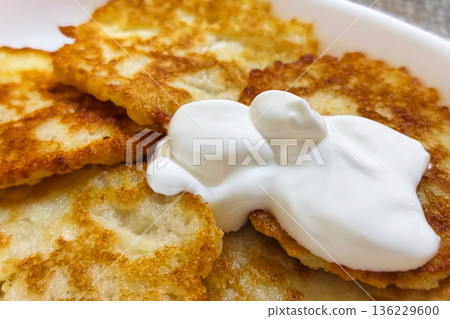 Potato pancakes are arranged on a plate with a generous dollop of sour cream on top. The setting appears casual and homey during an afternoon meal 136229600