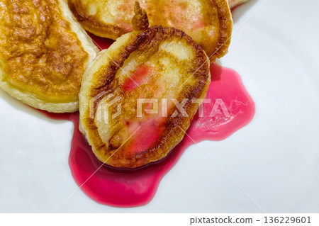 Pancakes sit on a white plate with red syrup pooled around them, ready to be eaten at breakfast or brunch with a focus on food presentation 136229601