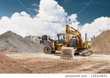 A wheel loader and a powerful excavator are visible at the construction site. Under a cloudy sky, heavy equipment can be seen working with piles of sand and gravel 136229641