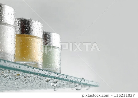 Glass tubes of cosmetic product with serum and cream on a glass shelf and water drops on a white background, bottom view. Skin care concept 136231027