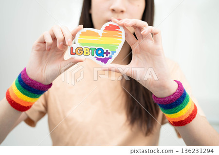 Asian woman holding LGBT heart with rainbow flag. Asian woman holding LGBT heart with rainbow flag. 136231294