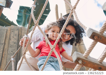 A cheerful mother encouraging her daughter playing together on a rope ladder in a public park - encouragement concept A cheerful mother encouraging her daughter playing together on a rope ladder in a public park - encouragement concept 136232223
