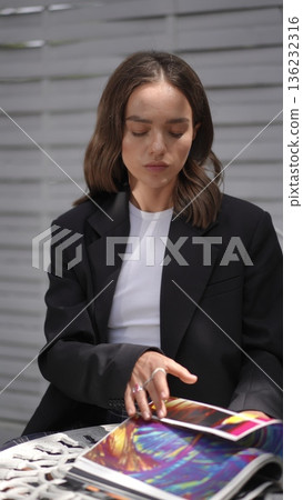 Elegant businesswoman sitting outdoors reading a colorful magazine Elegant businesswoman sitting outdoors reading a colorful magazine 136232316