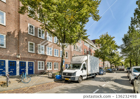 A scenic street featuring a mix of modern and historic buildings, lined with trees and parked vehicles, showcasing urban life and architecture. 136232498