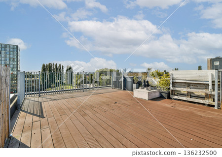 A contemporary rooftop terrace featuring wooden flooring, greenery, and a clear view of the urban skyline under a bright sky with scattered clouds. A contemporary rooftop terrace featuring wooden flooring, greenery, and a clear view of the urban skyline under a bright sky with scattered clouds. 136232500