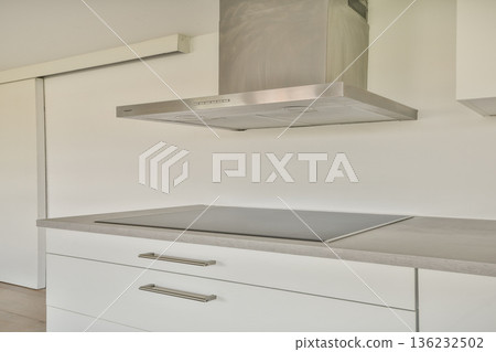 A minimalist kitchen featuring a sleek countertop, a stylish range hood, and clean lines, ideal for contemporary living. 136232502