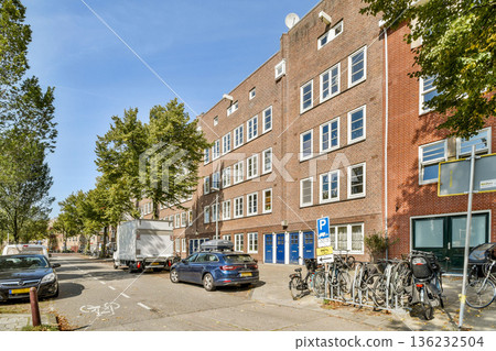 A picturesque street scene featuring vibrant trees, parked cars, and bicycles along a historic building in an urban setting. 136232504