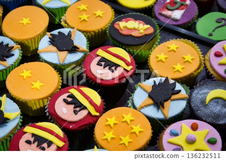 Lots of cupcakes with colorful designs on top on a baking tray 136232511