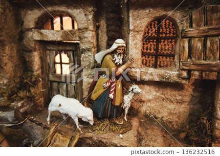 Close-up of a nativity scene figurine of a shepherd with sheep in a street with houses 136232516