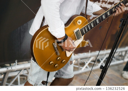 A musician on stage playing of gold colored electric guitar 136232526