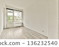 An empty room featuring large windows allowing ample natural light. The light wooden flooring complements the clean, white walls, creating a serene atmosphere. 136232540