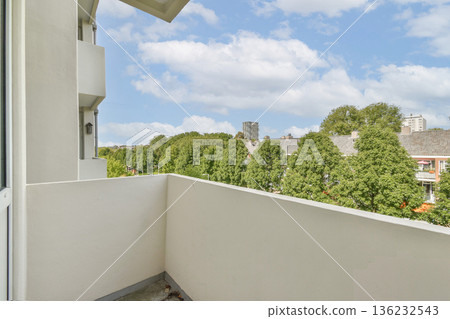 A well-designed balcony with a view of vibrant green trees and urban architecture in the background. Ideal for relaxation and enjoying nature in an urban setting. A well-designed balcony with a view of vibrant green trees and urban architecture in the background. Ideal for relaxation and enjoying nature in an urban setting. 136232543