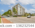 A modern residential building surrounded by greenery and a clear blue sky. The vibrant scene showcases urban living with a hint of nature. 136232544
