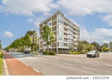 A modern residential building surrounded by greenery and a clear blue sky. The vibrant scene showcases urban living with a hint of nature. 136232544