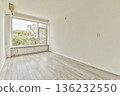 A spacious, uncluttered room featuring large windows that flood the space with natural light, showcasing a pale wooden floor and neutral walls. 136232550