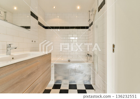 A sleek and contemporary bathroom featuring white tiled walls, a wooden vanity, and stylish black and white flooring. Perfect for design inspiration and home decor ideas. 136232551