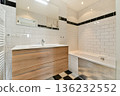 A sleek modern bathroom design featuring white tiled walls, a wooden vanity, and a bathtub. The space is illuminated with soft lighting for a cozy feel. 136232552