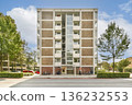 A striking modern building stands tall in an urban environment, flanked by lush trees and clear skies, showcasing contemporary architecture and urban design. 136232553