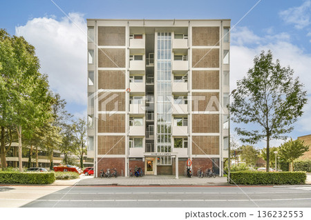 A striking modern building stands tall in an urban environment, flanked by lush trees and clear skies, showcasing contemporary architecture and urban design. 136232553
