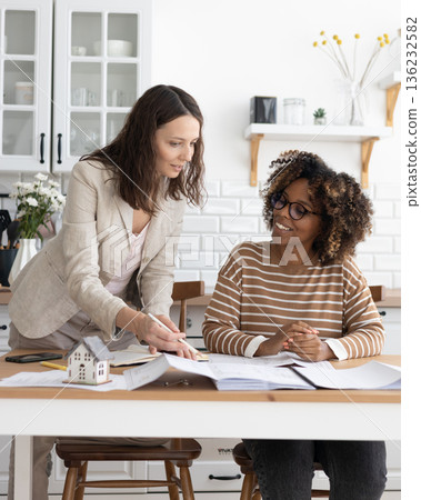 business person sitting at table, negotiating. two women going through papers, discussing project. business person sitting at table, negotiating. two women going through papers, discussing project. 136232582