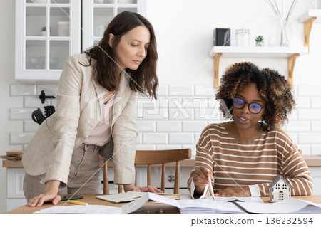 business person sitting at table, negotiating. two women going through papers, discussing project. business person sitting at table, negotiating. two women going through papers, discussing project. 136232594