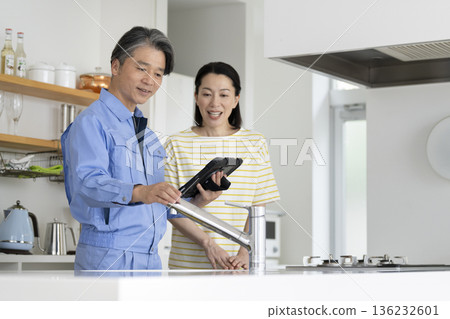一位中年婦女和一名承包商正在檢查廚房管道。 一位中年婦女和一名承包商正在檢查廚房管道。 136232601