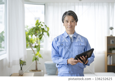 A man in his 50s wearing work clothes and holding a tablet. Housing-related contractor image. Portrait. Looking at the camera. A man in his 50s wearing work clothes and holding a tablet. Housing-related contractor image. Portrait. Looking at the camera. 136232625