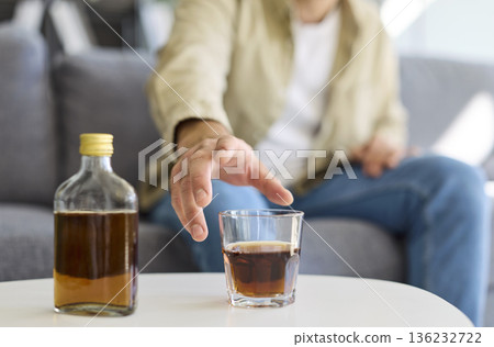 Man drinking whiskey on couch, reflecting alcohol addiction and health risks Man drinking whiskey on couch, reflecting alcohol addiction and health risks 136232722