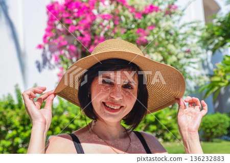 A brunette in a summer hat under the bright sun of Egypt against the backdrop of blooming greenery A brunette in a summer hat under the bright sun of Egypt against the backdrop of blooming greenery 136232883