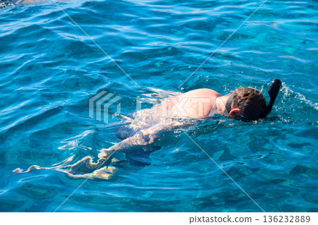 A man in a mask floats on the surface of the Red Sea and looks into the depths A man in a mask floats on the surface of the Red Sea and looks into the depths 136232889