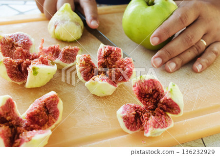 Close-up shot of peeled figs cut up into quarters, showing the red seeds inside, a person's hand on a chopping board with a knife Close-up shot of peeled figs cut up into quarters, showing the red seeds inside, a person's hand on a chopping board with a knife 136232929