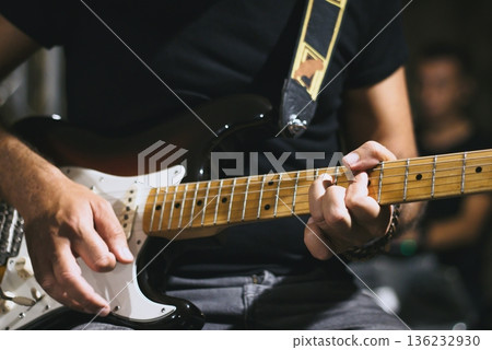 Close-up of a man's hands playing a chord on a sleek shaped electric guitar with a maple neck - live music band performance on stage Close-up of a man's hands playing a chord on a sleek shaped electric guitar with a maple neck - live music band performance on stage 136232930
