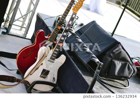 A couple of electric guitars leaning against a stand next to a live performance stage A couple of electric guitars leaning against a stand next to a live performance stage 136232934