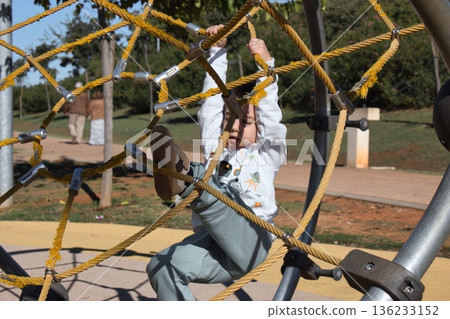 A white Caucasian boy in an outdoor play park, playing on a climbing frame A white Caucasian boy in an outdoor play park, playing on a climbing frame 136233152