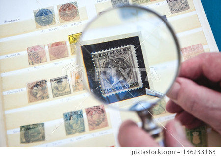 A close-up view of an old Canadian stamp through the lens of a magnifying glass, part of a collection book 136233163