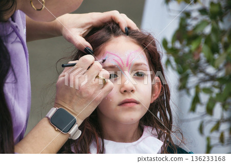 A white Caucasian woman face-painting a young girl for carnival A white Caucasian woman face-painting a young girl for carnival 136233168