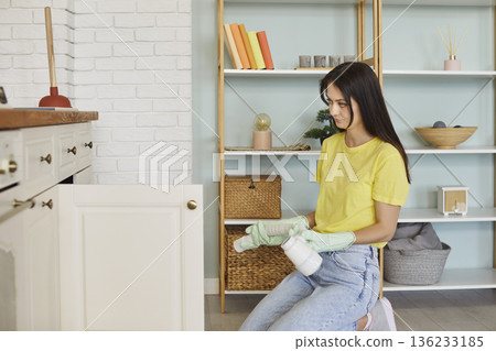 Woman housewife sitting near open kitchen cabinet, domestic care, holding cleaning supplies, spray 136233185