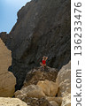 Woman, swimsuit, rocks. Relaxing woman in red swimsuit sits on large rocky beach under bright blue sky, copy space. 136233476