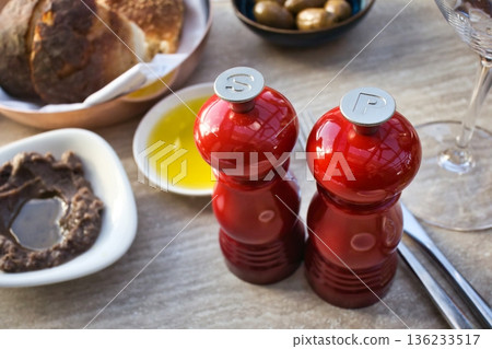 Fancy red stylish salt and pepper grinders with the letters "S" and "P" on a table with oil, bread, olives and bigilla dip 136233517