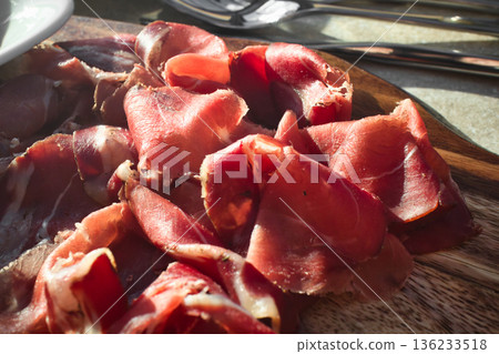 Close-up of thin slices of wild boar prosciutto laid out on a wooden chopping board 136233518