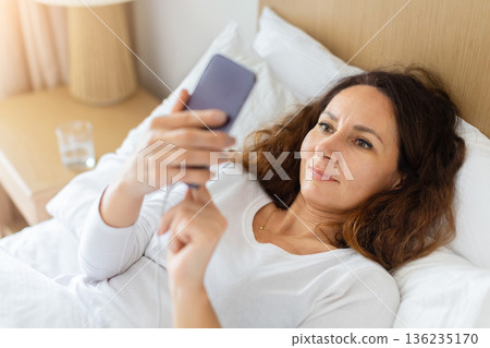 Middle aged caucasian woman lying in bed at home using smartphone 136235170