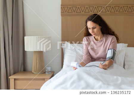 Caucasian middle aged woman measuring blood pressure at home using digital monitor 136235172